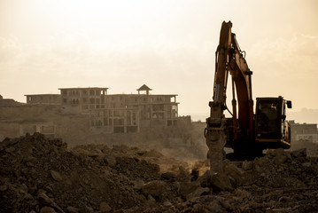 silhouette of Excavator loader at construction site with raised bucket over sunset.Heavy construction equipment