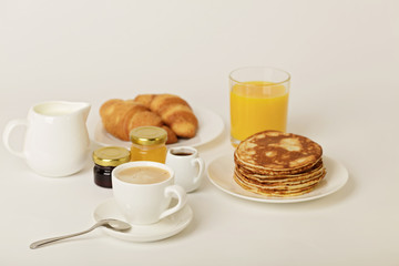 Breakfast - coffee with croissants, juice with pancakes on a white background.