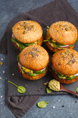 Healthy baked sweet potato burger with whole grain bun, guacamole, vegan mayonnaise and vegetables on a black slate board. Vegetarian food concept, dark background.