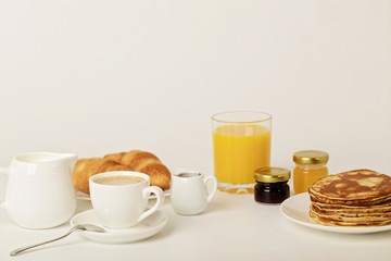 Breakfast - coffee with croissants, juice with pancakes on a white background.