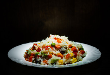 Rice with mixed vegetables on white plate  
 on dark wooden background with copy space.