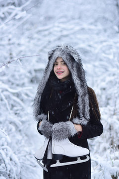 Girl smile with figure skates at trees in snow
