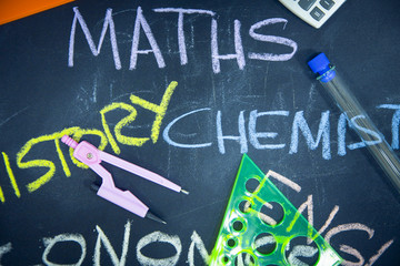 Education concept: Names of school subjects inscribed on a black chalkboard with colored chalks and stationary, close up, top view