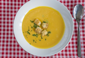 health eating concept/white plate with pumpkin soup and spoon on red and white chekered tablecloth top view