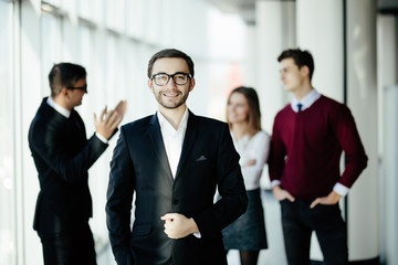 Smiling and confident business man standing in front of discussing team in office