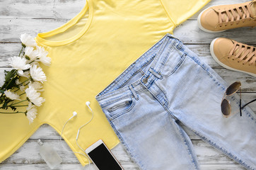 Womens fashion clothing, shoes, accessories (beige leather sneakers, blue jeans, yellow top (t-shirt) headphones, cell phone, perfume, sunglasses. Fashion. View above. Spring summer collection