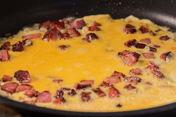 Cookin homemade omelette in the frying pan with salami