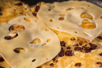 Cookin omelette in the frying pan with salami and cheese