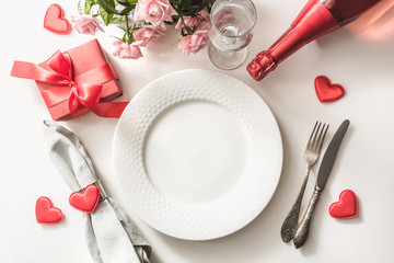 Valentines day dinner with table place setting with red gift, glass for champagne, a bottle of...