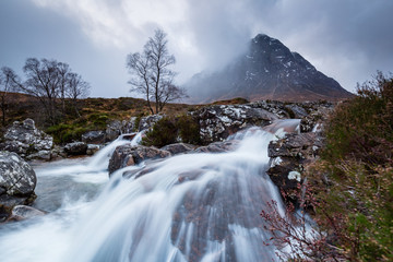 landscape view of scotland and buchaille etive mor with a flowing waterfall and river in the foreground in winter in the highlands of scotland