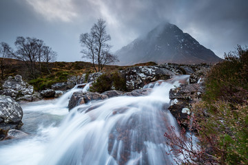 landscape view of scotland and buchaille etive mor with a flowing waterfall and river in the foreground in winter in the highlands of scotland