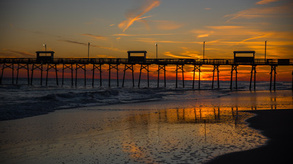Obraz premium Colorful Sunset at ocean coast with silhouette of pier and photographer