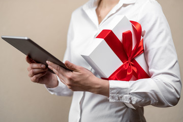 A woman in a white shirt is holding a silver tablet and a white gift box under her arm