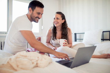Happy couple using laptop on bed in the bedroom.
