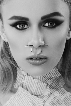 Monochrome closeup beauty art portrait of young beautiful woman blond girl with long straight hair with natural makeup, piercing in nose, newspapers on body. Hairstyle, skincare and cosmetics concept