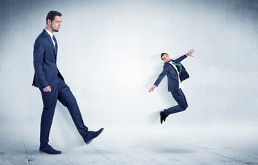 Big businessman kicking small businessman