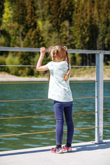 A little girl stands and looks at the lake and the forest. Concept childhood, lifestyle, vacation, travel.