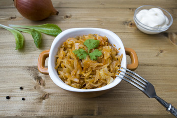 Appetizing stewed cabbage, sour cream, onion and lettuce leaves on a wooden background.