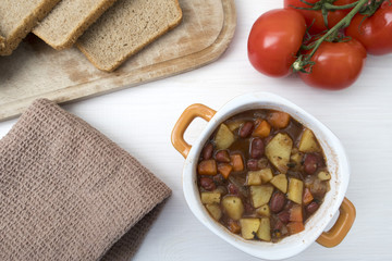 Appetizing beautiful soup with potatoes, onions, carrots and beans. Tomatoes and bread. Top view, against a light background.