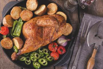 fried chicken half with potatoes and tomatoes in the frying pan