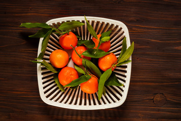 mandarins with green leaves in a white authentic vase for fruit on a dark wooden background