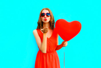 Portrait pretty woman sends an air kiss with red air balloons on blue background