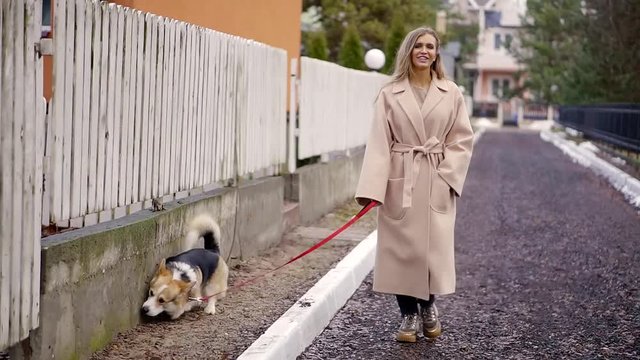 Stylish blonde walking his dog and did not notice how the animal village to defecate in the toilet on the lawn at the fence of the house.