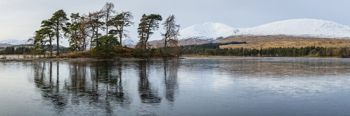 landscape view of scotland and trees at the edge of a frozen loch tulla in the remote highlands of scotland