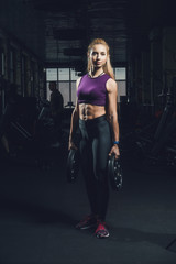 Close-up portrait of muscular young girl training with barbells in the gym. Brutal athletic girl with a six-pack, perfect abs, shoulders, biceps, triceps and chest	