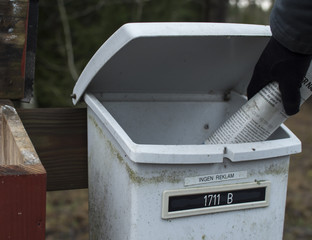 Old white mailbox in the woods, with a gloved hand delivering a newspaper