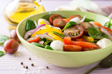 Fresh salad with spinach, bell peppers, tomatoes, red onions and mozzarella on purple wooden background.