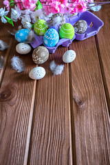 Painted Easter eggs with feathers and a branch of sakura on a dark wooden background