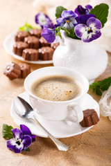 Postcard with cup of cooffee, chocolate candies in flower shape and pansy. Holiday food concept.