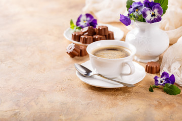 Postcard with cup of cooffee, chocolate candies in flower shape and violets. Holiday food concept with copy space.