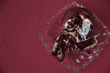 Ripe pomegranate on a glass plate on a red background. Diet and organic food concept