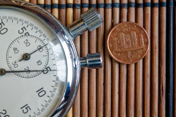 Euro coin with a denomination o one euro cents and stopwatch on wooden table - back side