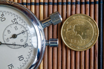 Euro coin with a denomination of fifty euro cents and stopwatch on wooden table - back side
