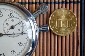 Euro coin with a denomination of twenty euro cents and stopwatch on wooden table - back side