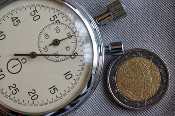 Euro coin with a denomination of two euro and stopwatch on gray denim backdrop - business background