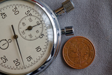 Obraz na płótnie Canvas Euro coin with a denomination of five euro cents (back side) and stopwatch on gray denim backdrop - business background