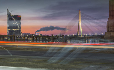 Sunset in Riga city with cars crossing the bridge creating light trails. Picturesque view on the highway with colorful sky. 