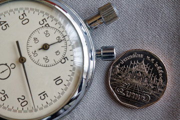 Thai coin with a denomination of 5 baht and stopwatch on gray denim backdrop - business background