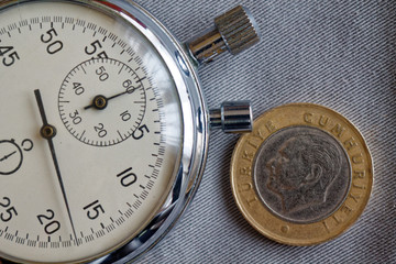 Turkish coin with a denomination of one lira (back side) and stopwatch on gray denim backdrop - business background