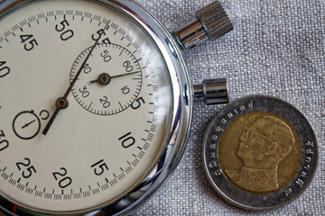 Thai coin with a denomination of ten baht (back side) and stopwatch on flax backdrop - business background