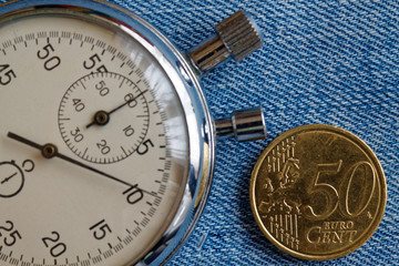 Obraz na płótnie Canvas Euro coin with a denomination of 50 euro cents and stopwatch on blue denim backdrop - business background