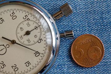 Obraz na płótnie Canvas Euro coin with a denomination of 5 euro cents and stopwatch on blue denim backdrop - business background