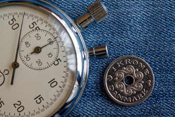 Denmark coin with a denomination of 1 krone (crown) and stopwatch on worn blue denim backdrop - business background