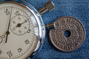 Denmark coin with a denomination of 5 krone (crown) and stopwatch on worn blue denim backdrop - business background