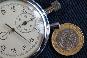 Turkish coin with a denomination of 1 lira and stopwatch on black jeans backdrop - business background