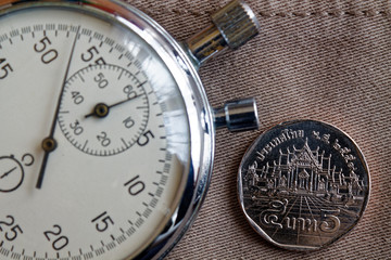 Thai coin with a denomination of 5 baht and stopwatch on old beige denim backdrop - business background
